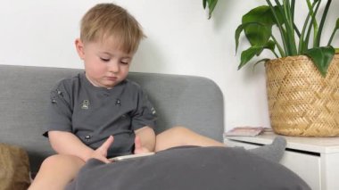Bir buçuk yaşındaki küçük bir çocuk odada oturuyor ve dikkatle cep telefonuna bakıyor, ki bu çocuğun gözlerine zararlı.