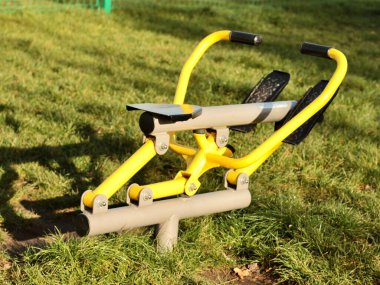 Şehirdeki yeşil çimlerin üzerinde kürek çeken sarı egzersiz makinesi.