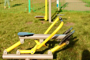 Şehirdeki yeşil çimlerin üzerinde kürek çeken sarı egzersiz makinesi.