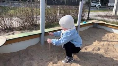 Bahar kıyafetleri içindeki küçük bir çocuk oyun parkındaki kum havuzunda tek başına oynuyor.