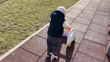 Küçük bir çocuk oyun parkında oynuyor, yolda yürüyen birini yuvarlıyor.
