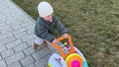 Küçük bir çocuk oynuyor, yolda bir bebek yürütecini yuvarlıyor.