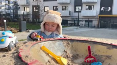 İki yaşında bir çocuk, oyun parkında oyuncak arabasıyla oyun oynuyor, çocuk ilkbaharın başında sıcak kıyafetler giyiyor.