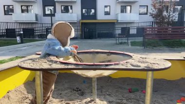 İki yaşında bir çocuk, oyun parkında oyuncak arabasıyla oyun oynuyor, çocuk ilkbaharın başında sıcak kıyafetler giyiyor.