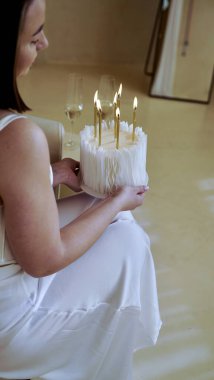 Kısa saçlı, beyaz elbiseli, elinde doğum günü pastası ve doğum günü için mumlar tutan tatlı bir genç kadın.