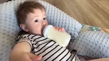 Kahverengi gözlü bir bebek yemek yiyor, küçük bir çocuk şişeden süt içiyor.