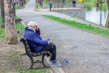 Polonya, Wroclaw, 13 Nisan 2025. Bastonlu yalnız yaşlı bir kadın parktaki bankta oturuyor..