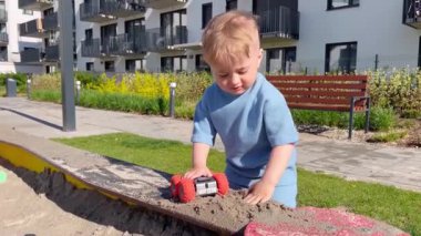 Küçük çocuk parkta bir oyuncakla oynuyor, kumları saçıyor.