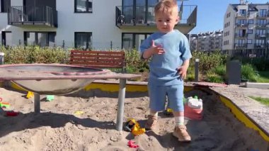 İki yaşındaki küçük bir çocuk oyun parkında kum havuzunda dikilirken kafasını karıştırıyor.