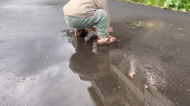 Kahverengi ayakkabılı küçük bir çocuk bahar yağmurundan sonra ayaklarını yere vurarak su sıçratıyor.