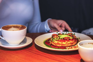 Restorandaki bir masada, soslu midyeli yumurta omleti ve beyaz bir tabakta bir kupa kahve sipariş edilir.