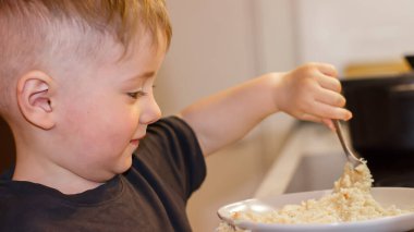 Küçük bir çocuk elinde kaşıkla akşamları mutfakta büyük bir kaseden yulaf lapası yiyor.