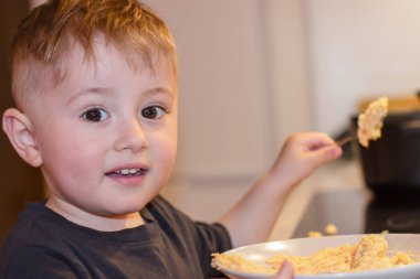 Küçük bir çocuk elinde kaşıkla akşamları mutfakta büyük bir kaseden yulaf lapası yiyor.