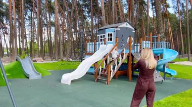 Çocuk parkında küçük bir çocuğu olan genç bir anne, kız fotoğrafçı, oyun evinin yanında slaytla oynayan çocuğun fotoğraflarını çekiyor.