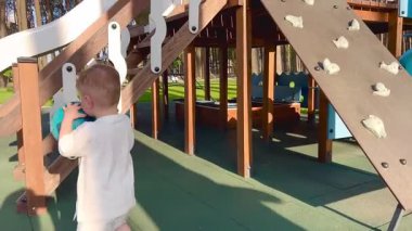 Elinde top olan küçük bir çocuk merdivenleri çıkmak için koşar, çocuk ormanın yakınındaki bir oyun alanında oynar.