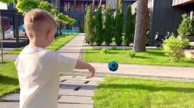 İki yaşında bir çocuk koşuyor ve bir topla oynuyor, küçük bir çocuk elinde topla avluda yürüyor..