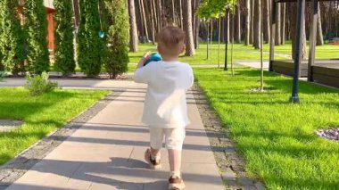 İki yaşında bir çocuk koşuyor ve bir topla oynuyor, küçük bir çocuk elinde topla avluda yürüyor..