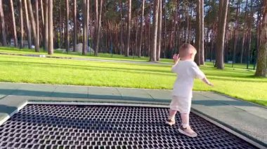  İki yaşında küçük bir çocuk atlıyor, eğleniyor, trambolinde sarkmış metal bir ağ üzerinde ormanın yakınındaki bir parkta.