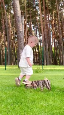  İki yaşında küçük bir çocuk atlıyor, eğleniyor, trambolinde sarkmış metal bir ağ üzerinde ormanın yakınındaki bir parkta.