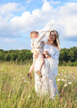 Annesinin kollarında küçük bir çocuk, çayırda eğleniyorlar, uçurtma uçuruyorlar.