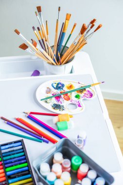 Çizim malzemeleri masaya serilmiştir: renkli kalemler, boyalar, fırçalar, paletler, renkli tebeşirler.