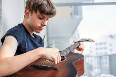 Bir genç hevesle gitar çalmayı öğrenir ve balkonda otururken boş zamanlarında telleri akort eder. Yüksek kalite fotoğraf