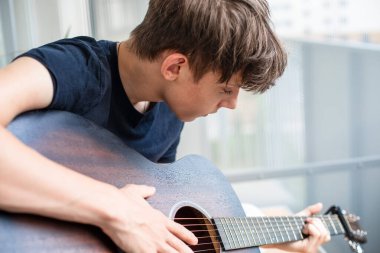 Bir genç hevesle gitar çalmayı öğrenir ve balkonda otururken boş zamanlarında telleri akort eder. Yüksek kalite fotoğraf
