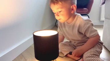 İki yaşında bir çocuk tehlikeli bir şekilde bir elektrik prizinin yanında oynuyor ve yetişkin denetimi olmadan bir lambayı yakıyor. Ev güvenliği kavramı, elektrik tehlikeleri ve çocuk korumanın önemi..