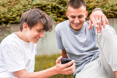 Parkta bir bankta oturan üç genç, akıllı telefonlar kullanarak dışarıda dinlenirken sosyal medyaya göz atıyorlar. Yüksek kalite fotoğraf