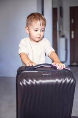 Elinde büyük siyah bir bavulla odanın ortasında duran çocuk seyahati, aile yolculuğunu ya da macerayı simgeliyor. Yüksek kalite fotoğraf