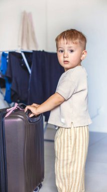Elinde büyük siyah bir bavulla odanın ortasında duran çocuk seyahati, aile yolculuğunu ya da macerayı simgeliyor. Yüksek kalite fotoğraf