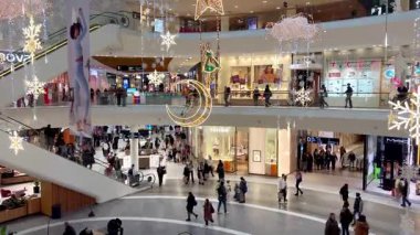 Polonya, Wroclaw, 12.12.2024. Noel tatilinden önce süslü bir alışveriş merkezi galerisi. Alışveriş yapanlar Noel ışıkları ve Noel süsleriyle modern bir ticaret merkezinde yürüyüp hediyeler alıyorlar. Tatil hazırlıklarının mevsimsel atmosferi.
