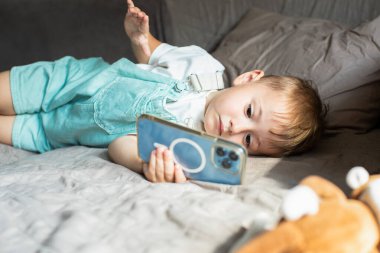 Genç bir çocuk evde modern çocukluk ve dijital eğlenceyi resmeden bir akıllı telefonda uzanıp çizgi film izliyor. Yüksek kalite fotoğraf