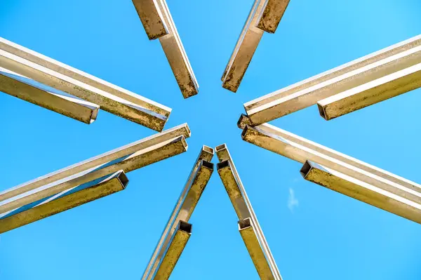 Geometric abstraction against the blue sky from several square metal pipes converging from different sides to the center of the photo