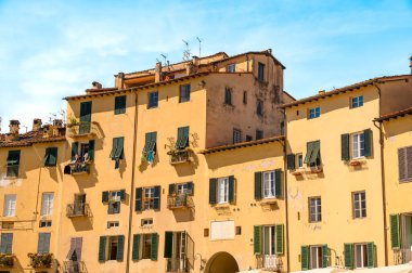 LUCCA, TUSCANY, ITALY - MAYIS 05, 2024: Güneşli bir günde mavi gökyüzüne karşı Piazza Anfiteatro 'da sarı bir binanın cephesi