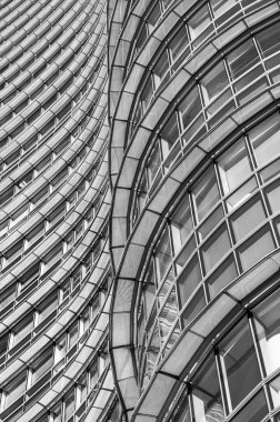 Pürüzsüz, yuvarlak metal ve cam çizgilerden oluşan bir cephenin geometrik soyutlaması. Dikey siyah beyaz fotoğraf