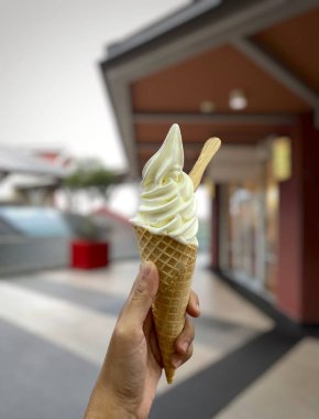 Pekalongan, Endonezya, 30 Ağustos 2023: arka planda bulanık bir külah dondurma tutuyorum. Bir Asyalının elinde dondurmanın fotoğrafı. Vanilyalı dondurma..