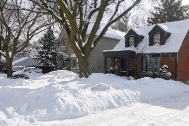 Toronto, ON, Kanada - 27 Şubat 2025: Banliyö evi çatıdan sarkan buz saçaklarıyla kaplı, güneş ışığı beyaz kış manzarasına gölge düşürürken,.