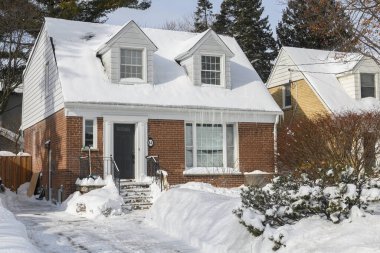 Toronto, ON, Kanada - 27 Şubat 2025: Banliyö evi çatıdan sarkan buz saçaklarıyla kaplı, güneş ışığı beyaz kış manzarasına gölge düşürürken,.