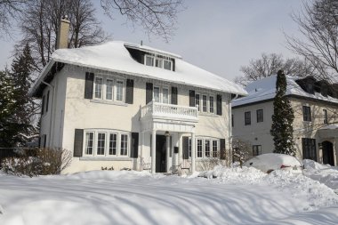 Toronto, ON, Kanada - 27 Şubat 2025: Banliyö evi çatıdan sarkan buz saçaklarıyla kaplı, güneş ışığı beyaz kış manzarasına gölge düşürürken,.