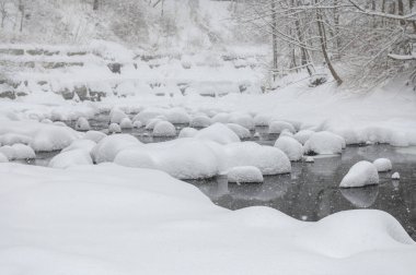 Yoğun karla kaplı büyük kayalar akan bir derede oturur ve yumuşak, yuvarlak şekilli eşsiz bir kış manzarası yaratır..