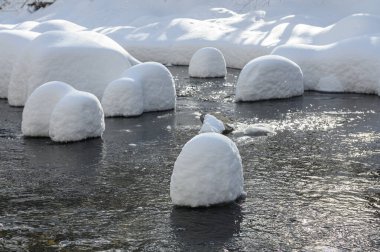 Yoğun karla kaplı büyük kayalar akan bir derede oturur ve yumuşak, yuvarlak şekilli eşsiz bir kış manzarası yaratır..