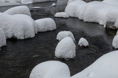 Yoğun karla kaplı büyük kayalar akan bir derede oturur ve yumuşak, yuvarlak şekilli eşsiz bir kış manzarası yaratır..