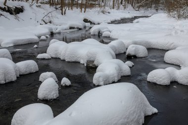 Yoğun karla kaplı büyük kayalar akan bir derede oturur ve yumuşak, yuvarlak şekilli eşsiz bir kış manzarası yaratır..
