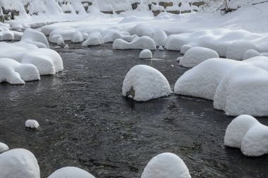 Yoğun karla kaplı büyük kayalar akan bir derede oturur ve yumuşak, yuvarlak şekilli eşsiz bir kış manzarası yaratır..