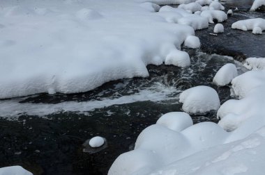 Yoğun karla kaplı büyük kayalar akan bir derede oturur ve yumuşak, yuvarlak şekilli eşsiz bir kış manzarası yaratır..