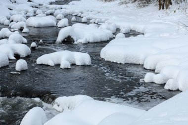 Yoğun karla kaplı büyük kayalar akan bir derede oturur ve yumuşak, yuvarlak şekilli eşsiz bir kış manzarası yaratır..