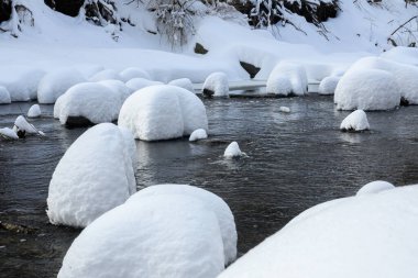 Yoğun karla kaplı büyük kayalar akan bir derede oturur ve yumuşak, yuvarlak şekilli eşsiz bir kış manzarası yaratır..