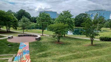 Charlotte, NC, ABD - 30 Nisan 2025: Modern ofis binaları yeşil çimenlerin, ağaçların ve Ballantyne Corporate Park 'ta bulutlu bir gökyüzünün altında bir yürüyüş yolunun ortasında duruyor.