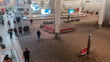 Toronto, ON, Kanada - 1 Mayıs 2025: Toronto Pearson Uluslararası Havalimanı 'ndaki insan, bagaj vagonu ve varış bilgileri sergilenen bir terminalin içini gösteren yüksek bir manzara.